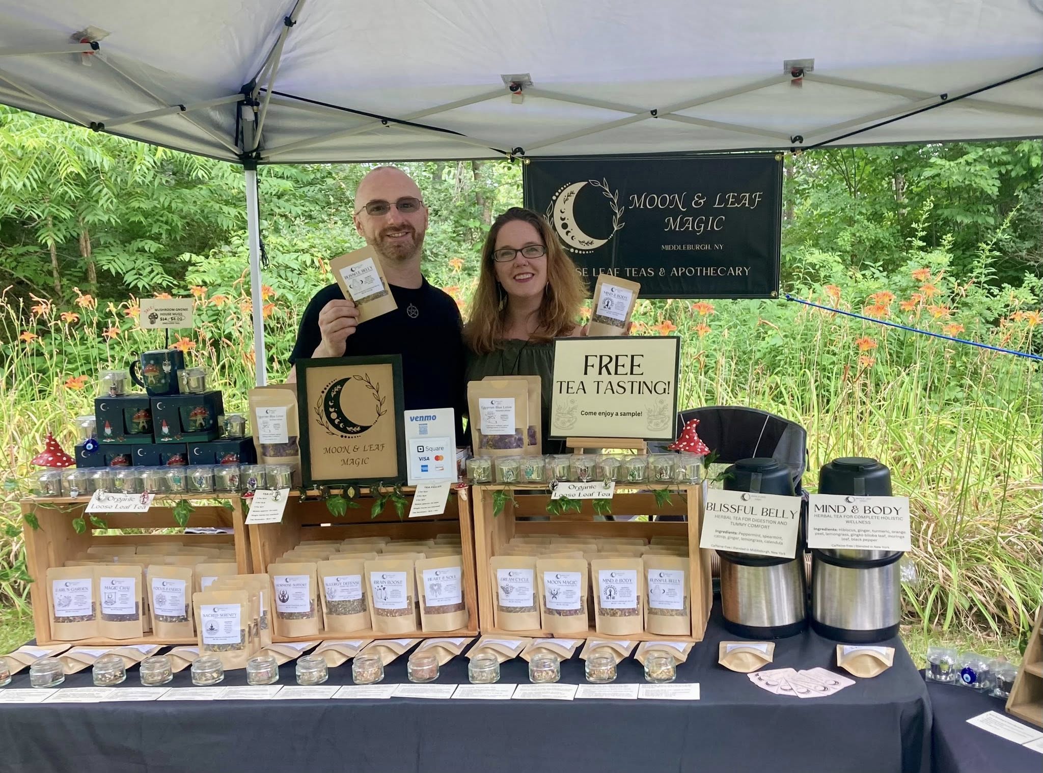 Davy & Tracy Russell of Moon & Leaf Magic pose behind their pop-up shop holding popular loose leaf tea blends.